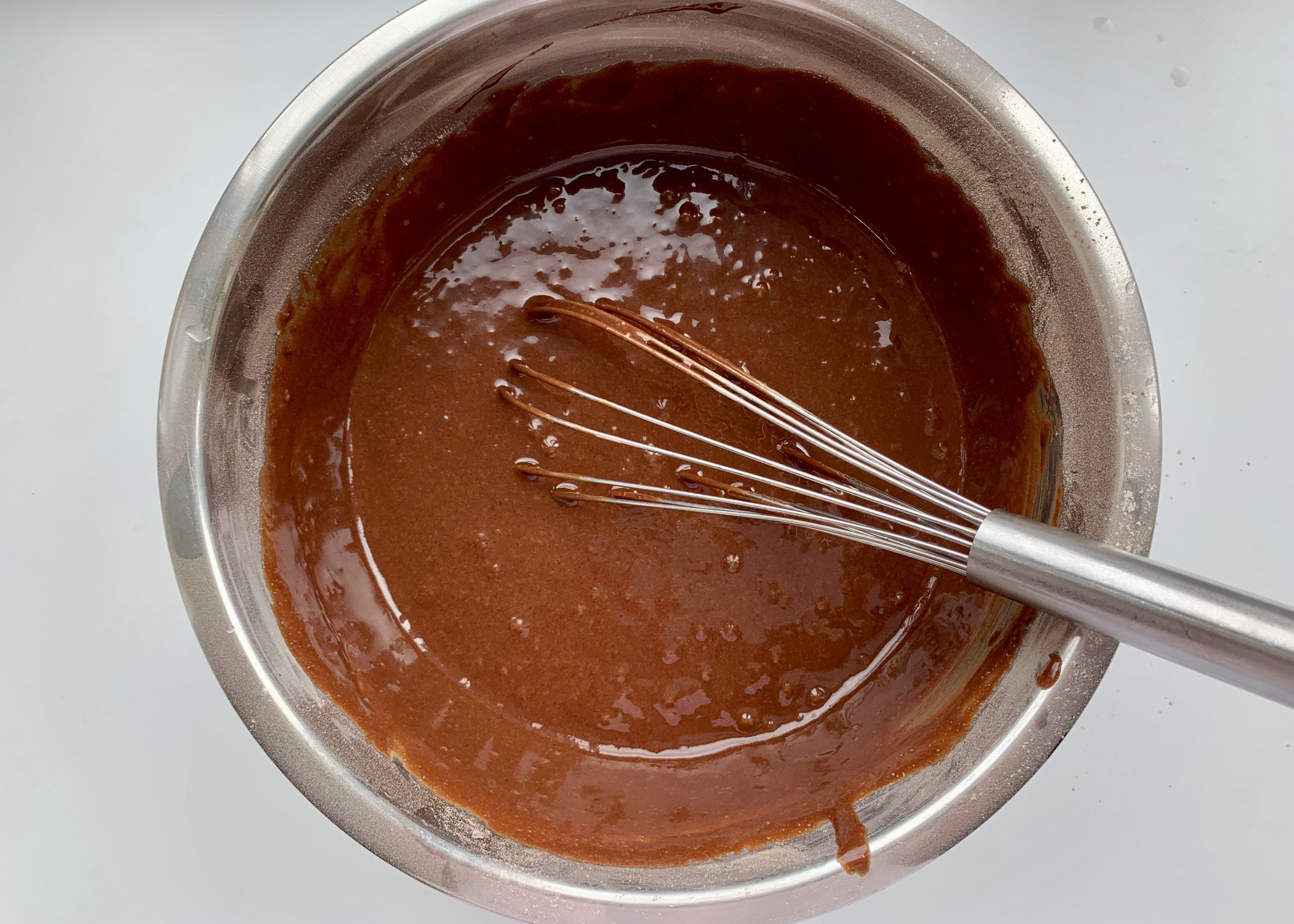 Gluten free chocolate muffin mixture in a stainless steel bowl with a whisk in 