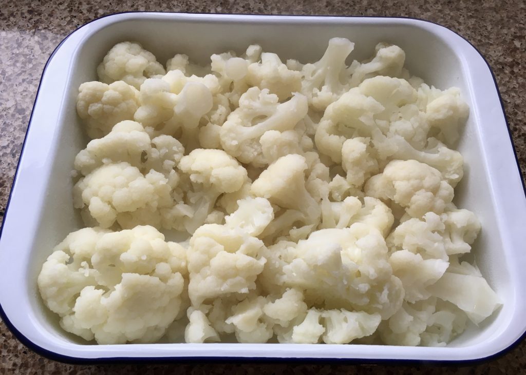 Cooked cauliflower in a white enamel oven tray