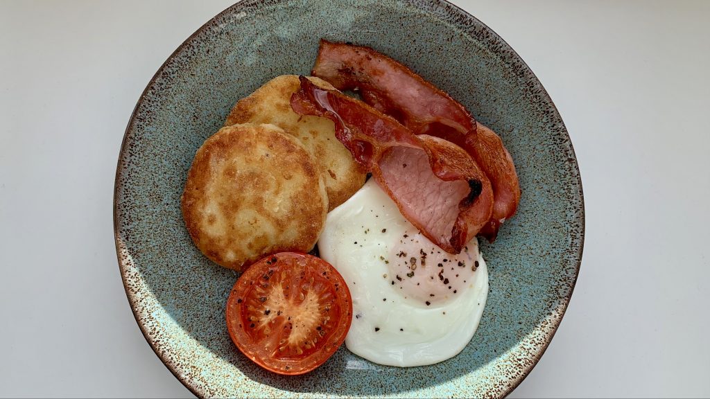 Gluten free potato cakes, bacon, fried egg and tomato in a blue bowl