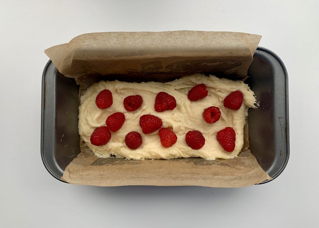 Sponge mixture in a 2lb loaf tin with raspberries scattered over the top