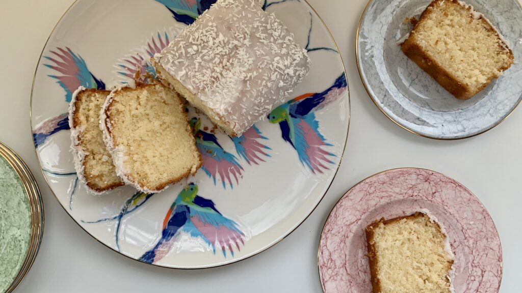 Gluten free iced coconut cake cut into slices on colourful plates