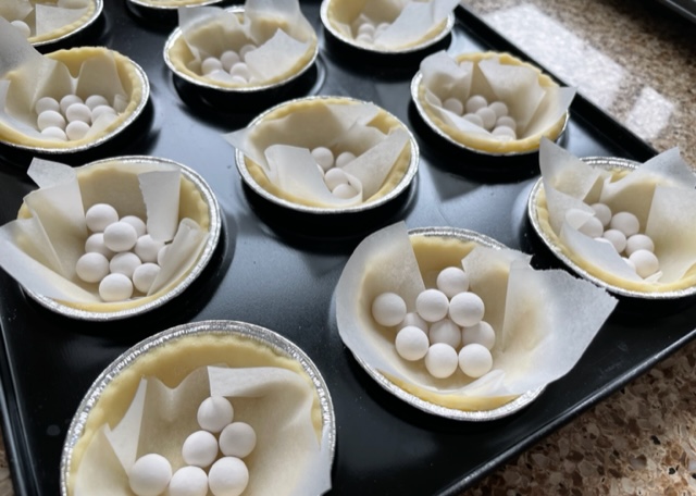 Gluten free tarts lined with greaseproof paper and filled with baking beans