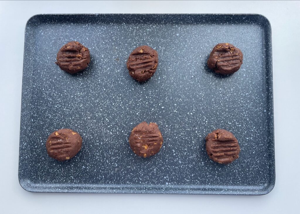 Balls of gluten free chocolate biscuit dough formed into balls on a baking tray and pressed down with a fork